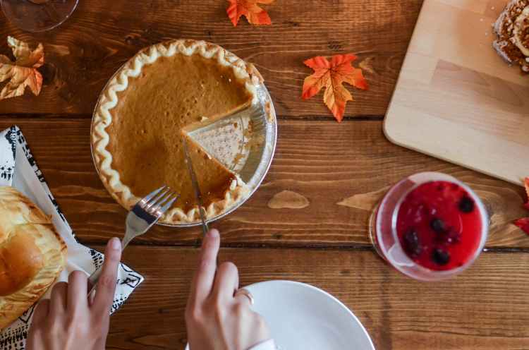 person holding knife and fork cutting slice of pie on brown wooden table